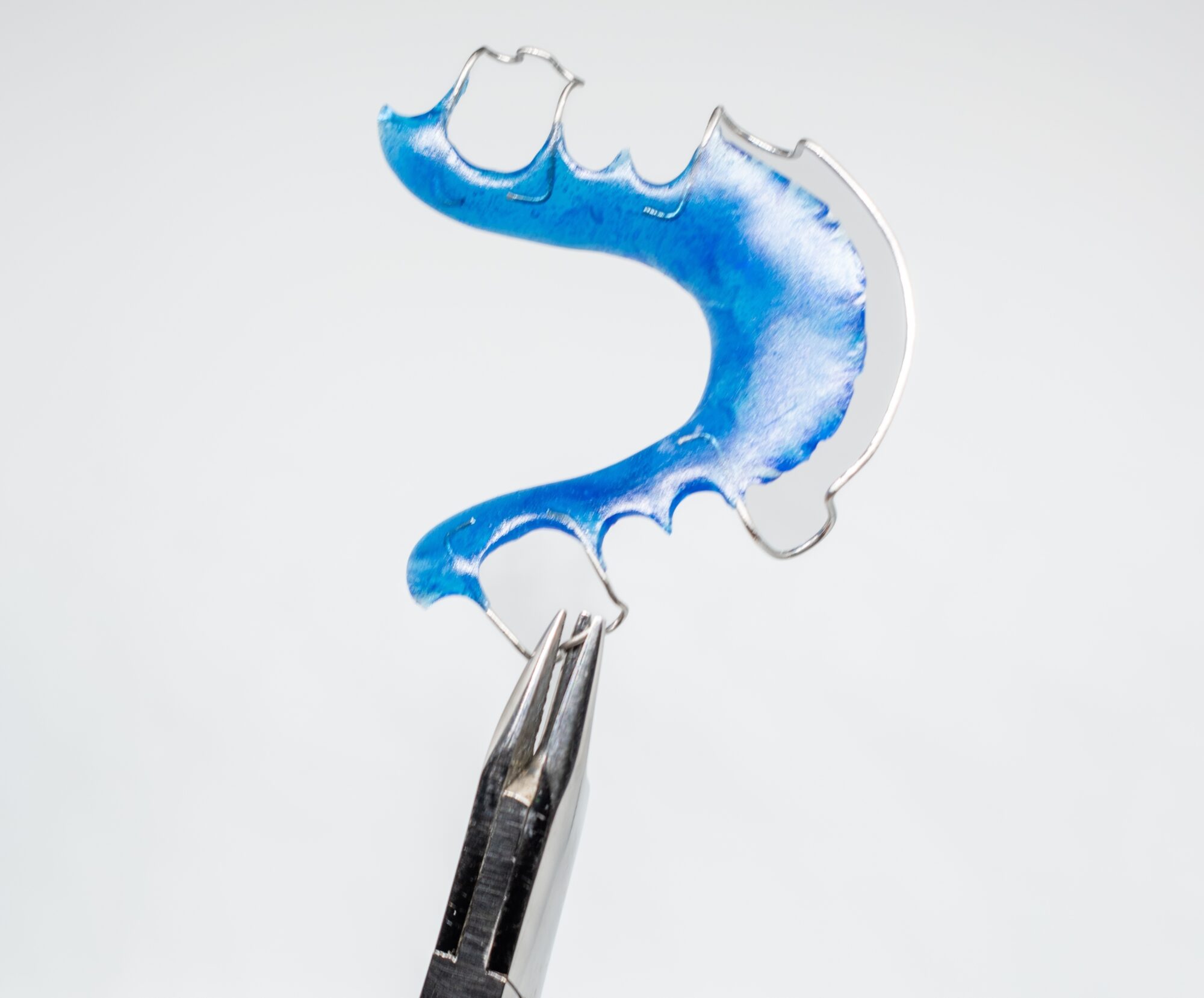 Blue Hawley retainer held by pliers, illustrating orthodontic appliance for maintaining teeth alignment after treatment.