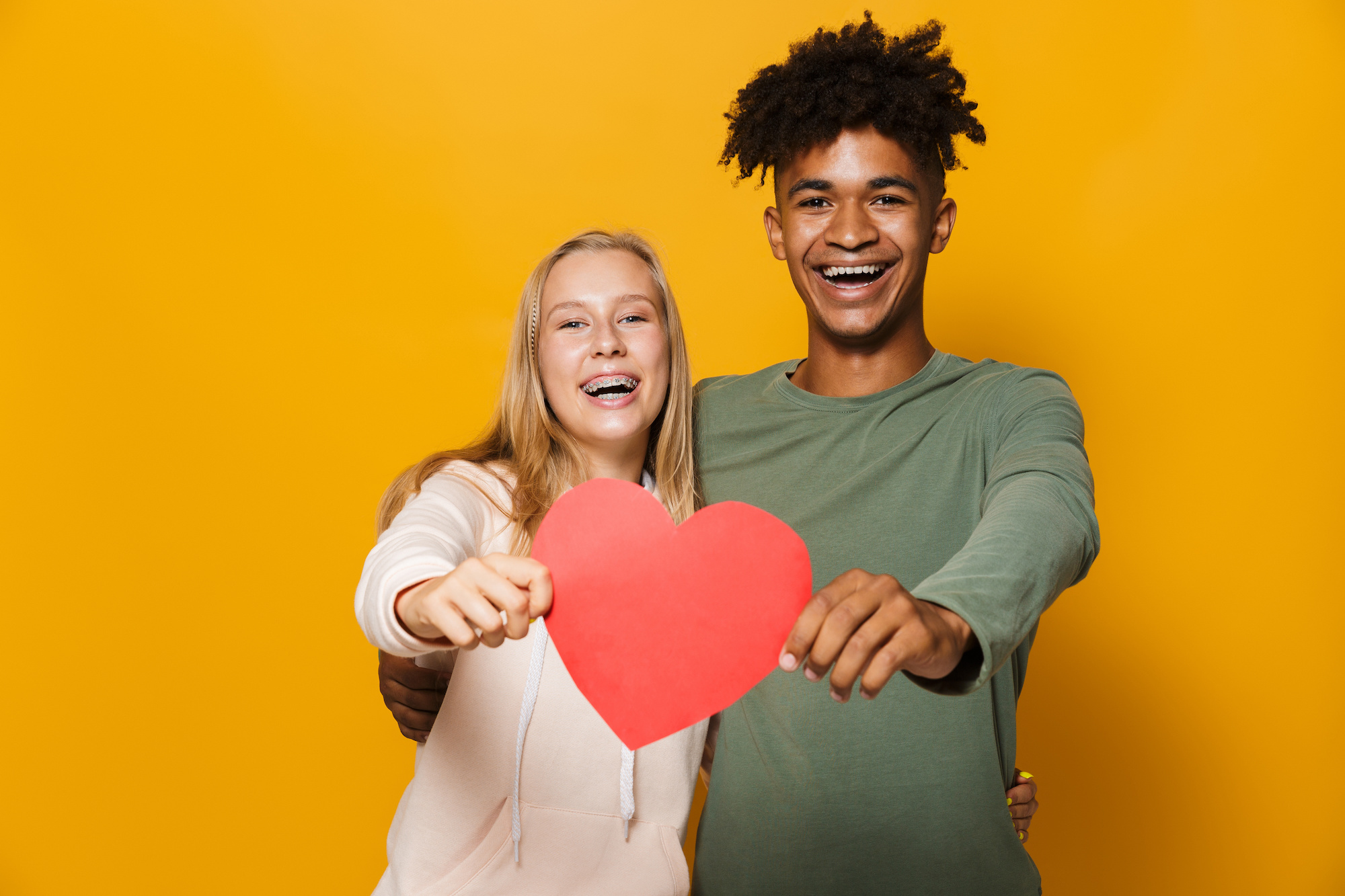 Photo of teenage friends man and woman 16-18 holding paper heart, isolated over yellow background grosse pointe farms braces