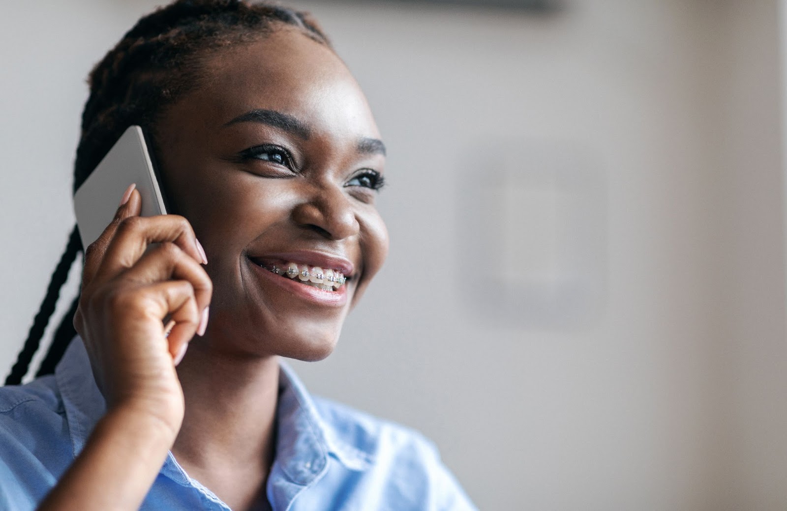 Smiling young woman with braces talking on a smartphone, emphasizing communication for orthodontic care.